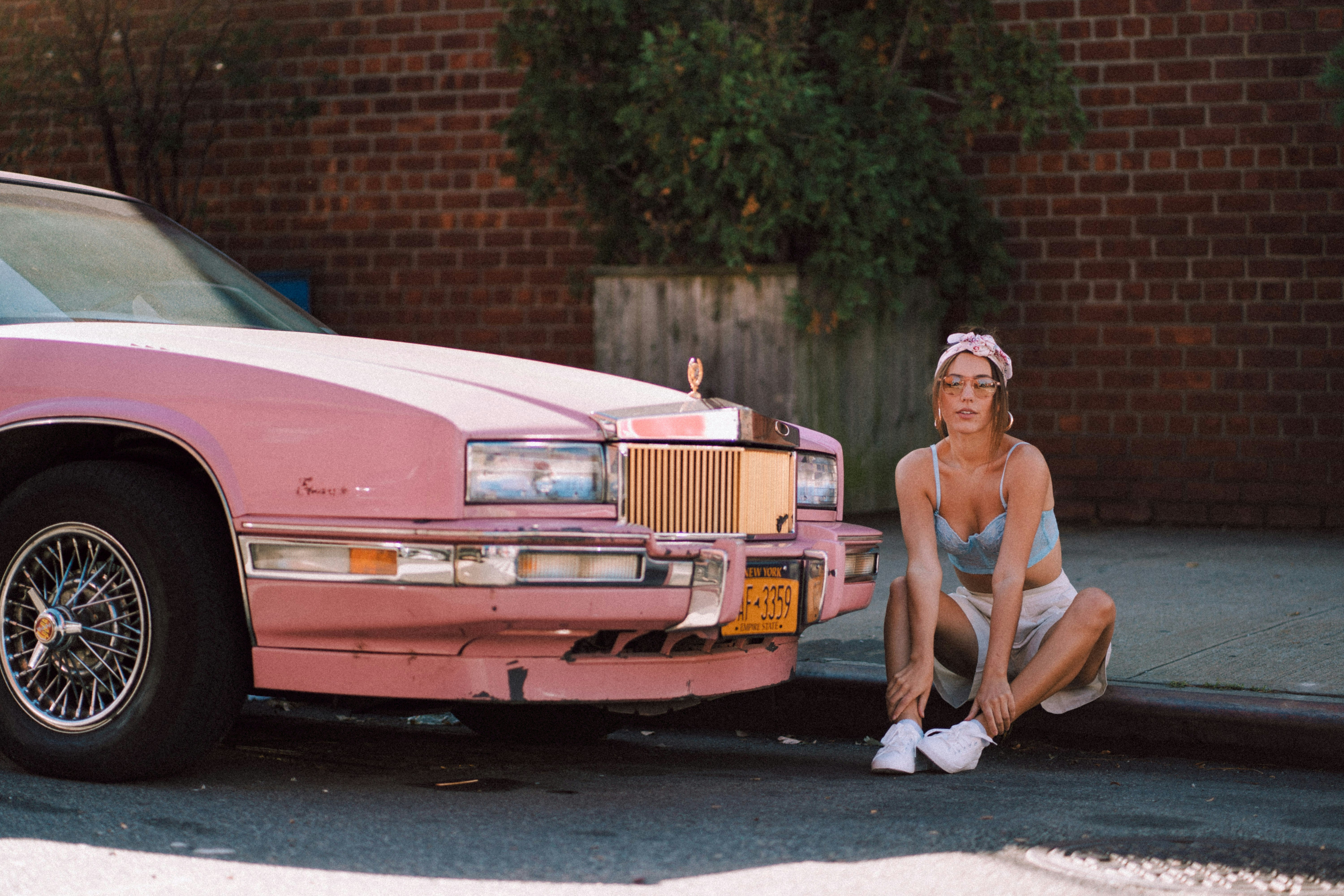 woman in white tank top and white pants leaning on red car